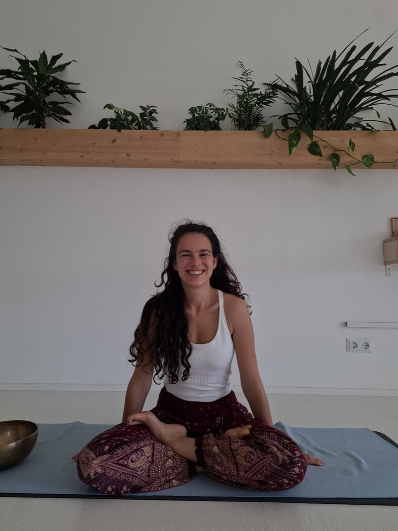 Nicole Schatz sitzt lächelnd auf ihrer Yogamatte